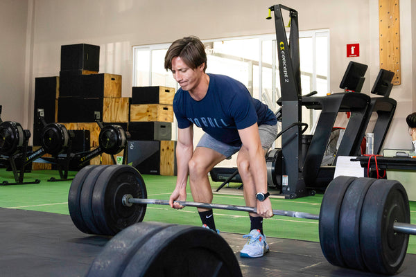 Person lifting weights in a gym setting with other people and equipment around